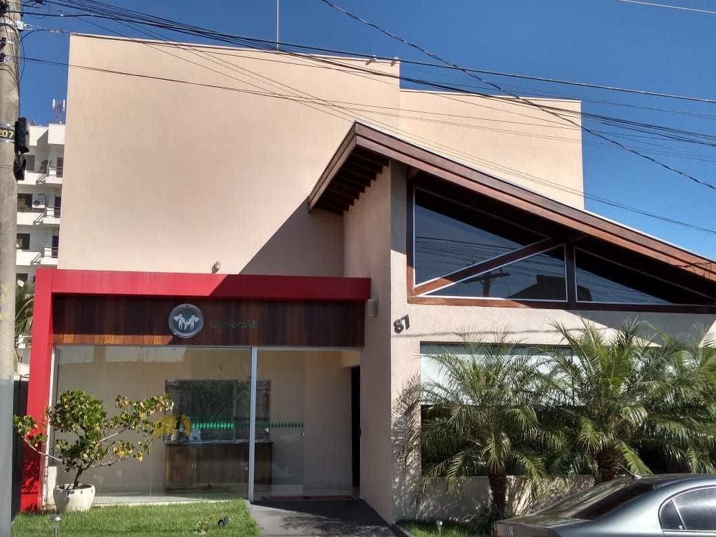 Un bâtiment moderne doté d’une grande fenêtre en verre, d’un auvent rouge et d’un palmier au premier plan.