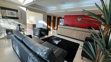 A hotel lobby with a reception desk, a black leather sofa, a coffee table, and a large plant.