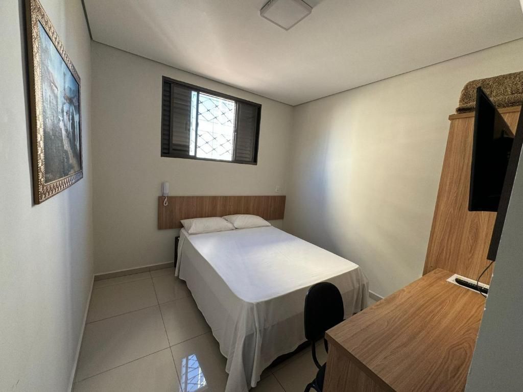 Un dormitorio pequeño y luminoso con una cama individual, un escritorio de madera y una ventana con persianas.