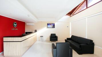 Un área de recepción con un mostrador de madera, un sofá de cuero negro y un televisor en la pared.