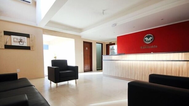 A reception area with a red wall, a reception desk, and black seating.