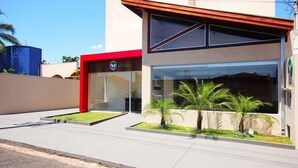 A modern building with a red entrance, large windows, and a well-maintained lawn with palm trees.