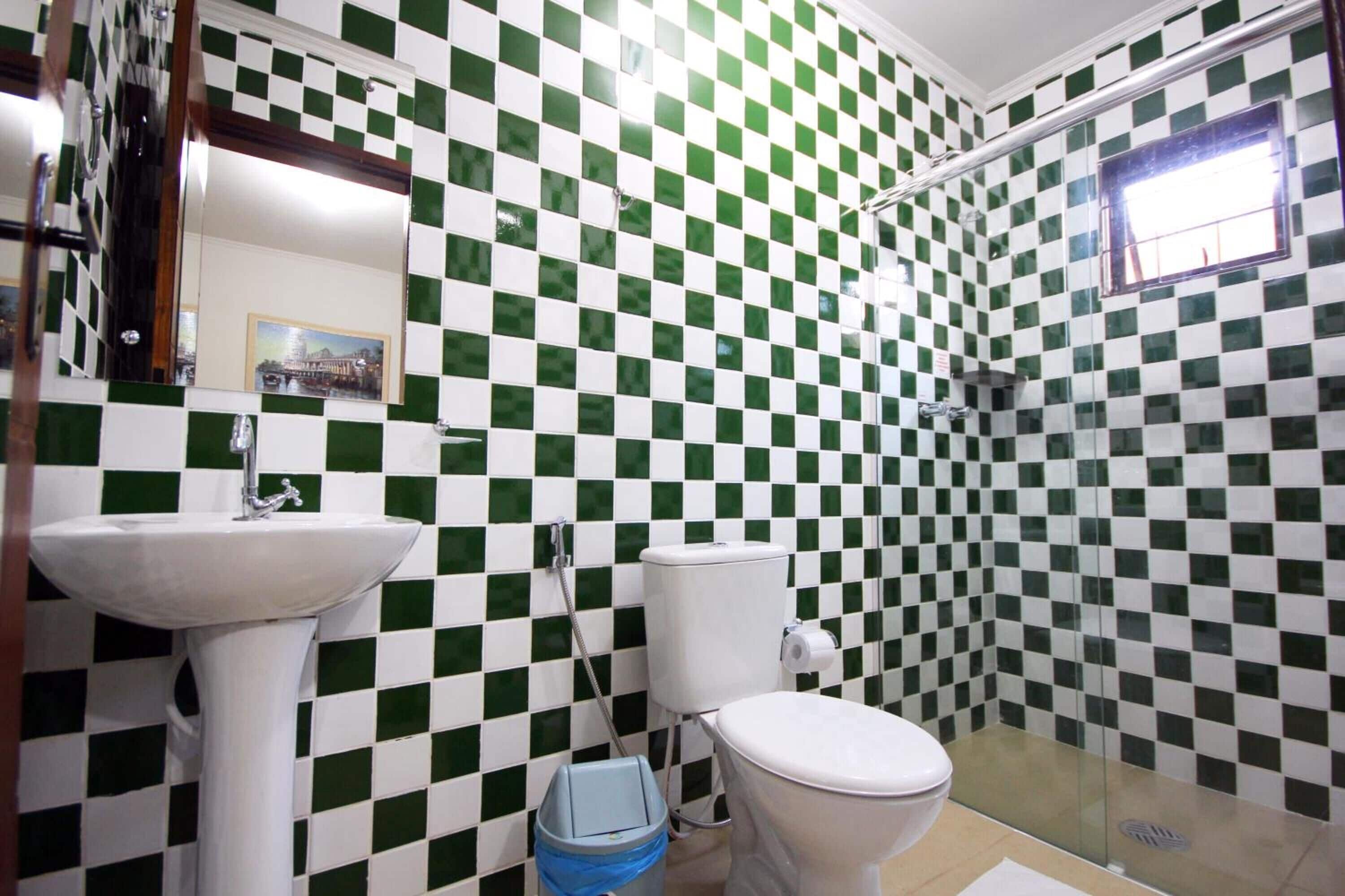 A bathroom with a checkered green and white tile wall, a white sink, a toilet, and a glass shower enclosure.