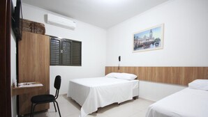 A hotel room with two single beds, a desk with a chair, a wooden wardrobe, and a painting on the wall.