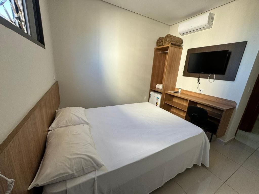 Habitación de hotel con cama, armario de madera, escritorio con silla y televisor de pantalla plana montado en la pared.
