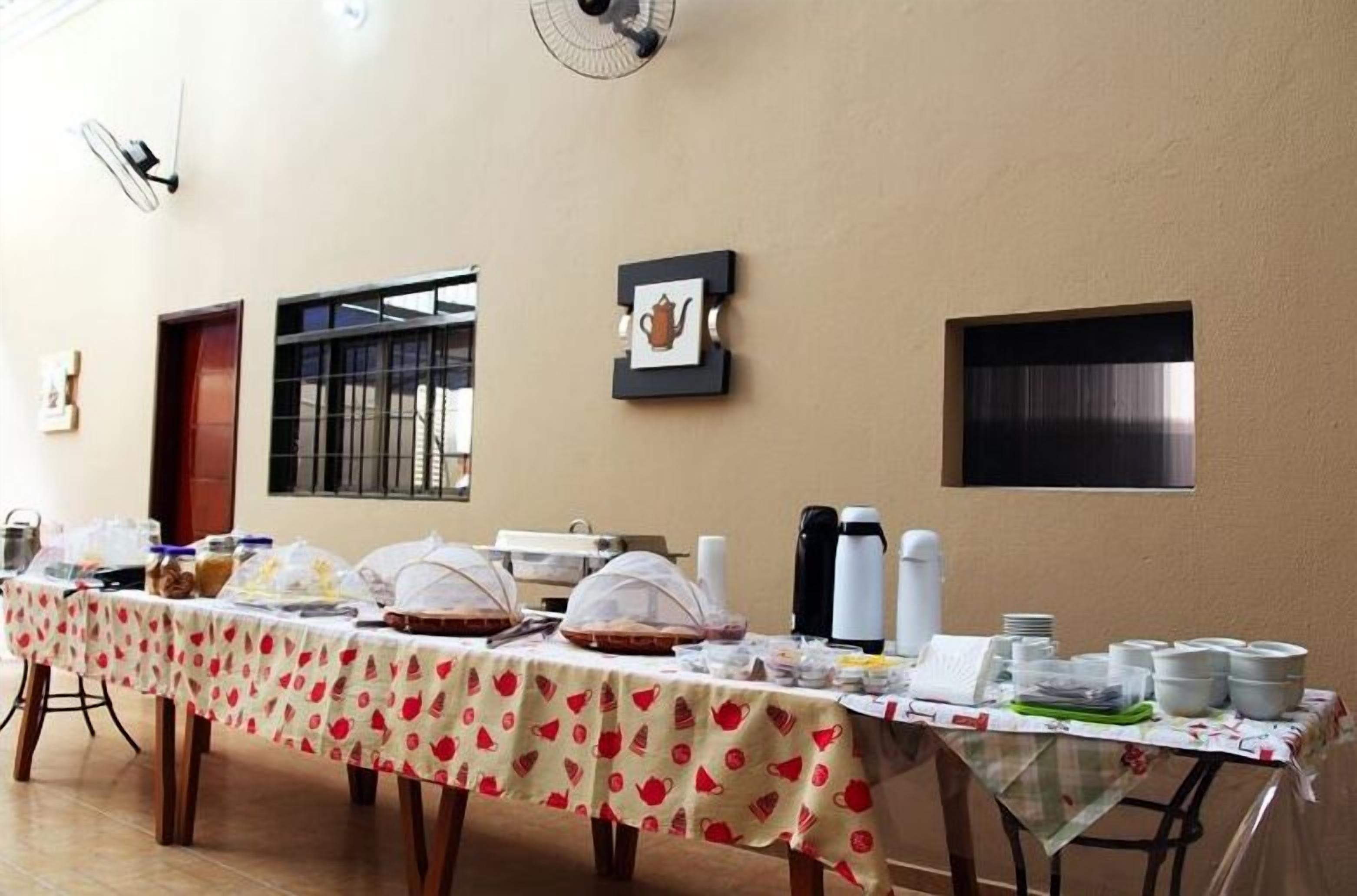 A long table with a tablecloth, covered food containers, and coffee makers.