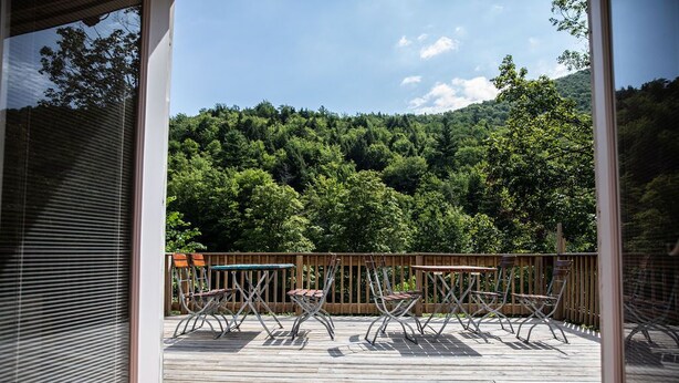 Eine Holzterrasse mit Metallstühlen und -tischen, mit Blick auf einen bewaldeten Hang.
