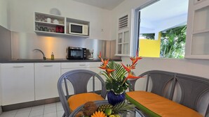 A modern kitchen with white cabinets, a microwave, and a coffee maker. There is a dining area with two chairs and a table, and a window with a view of greenery. - Domaine de May (Saint-François)