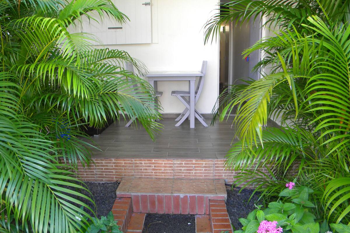 Ein Terrassenbereich mit Tisch und Stühlen, umgeben von üppiger Bepflanzung und einer Ziegelkante.