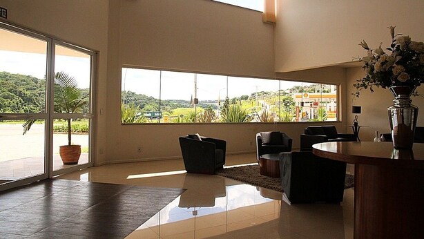 A spacious room with a large window offering a view of greenery and buildings. There are several chairs and a table with a vase of flowers. - Lazuli Hotel (Itatiba)