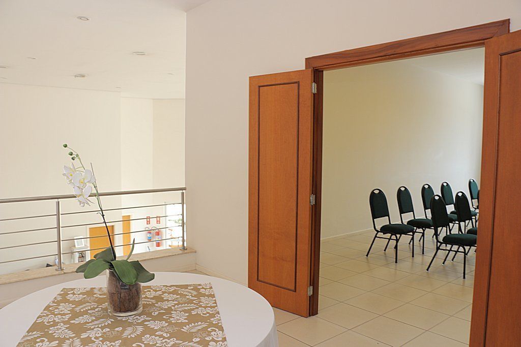 A room with a round table, a potted orchid, and a view of a balcony with chairs.