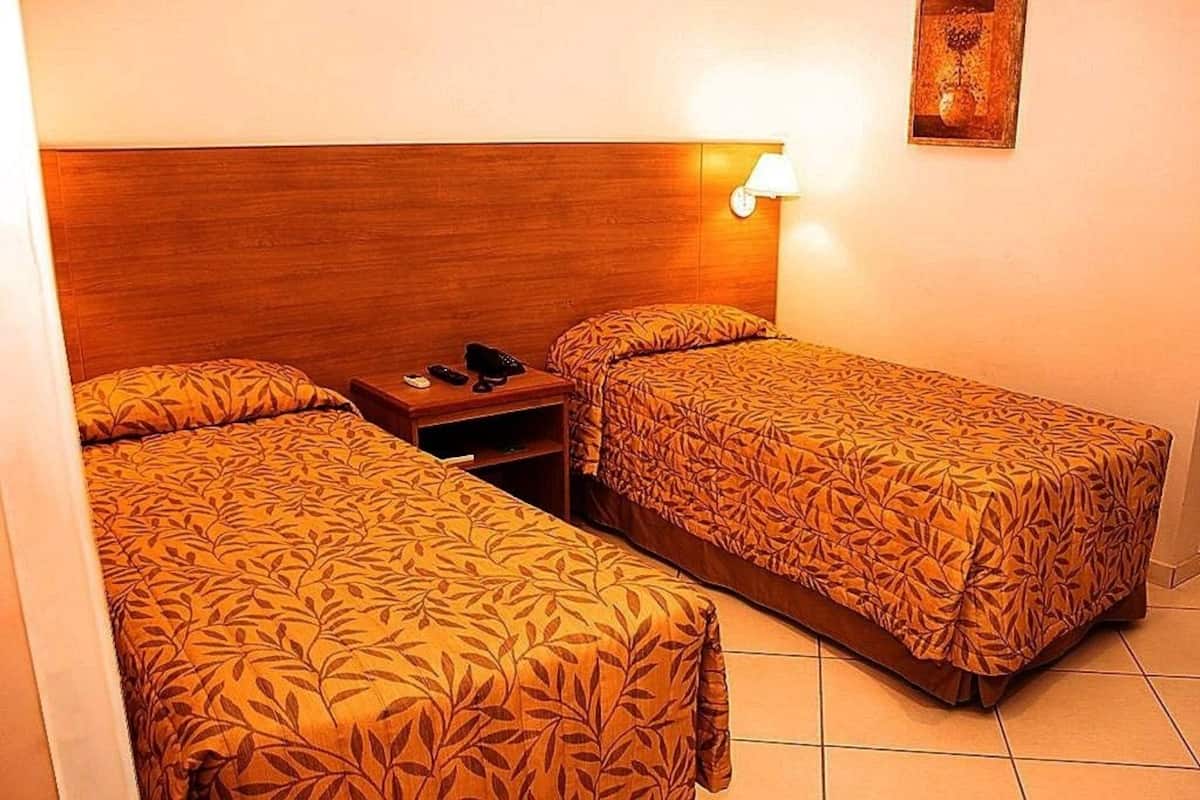 A room with two single beds, a wooden headboard, a nightstand with a lamp, and a small table with a telephone.