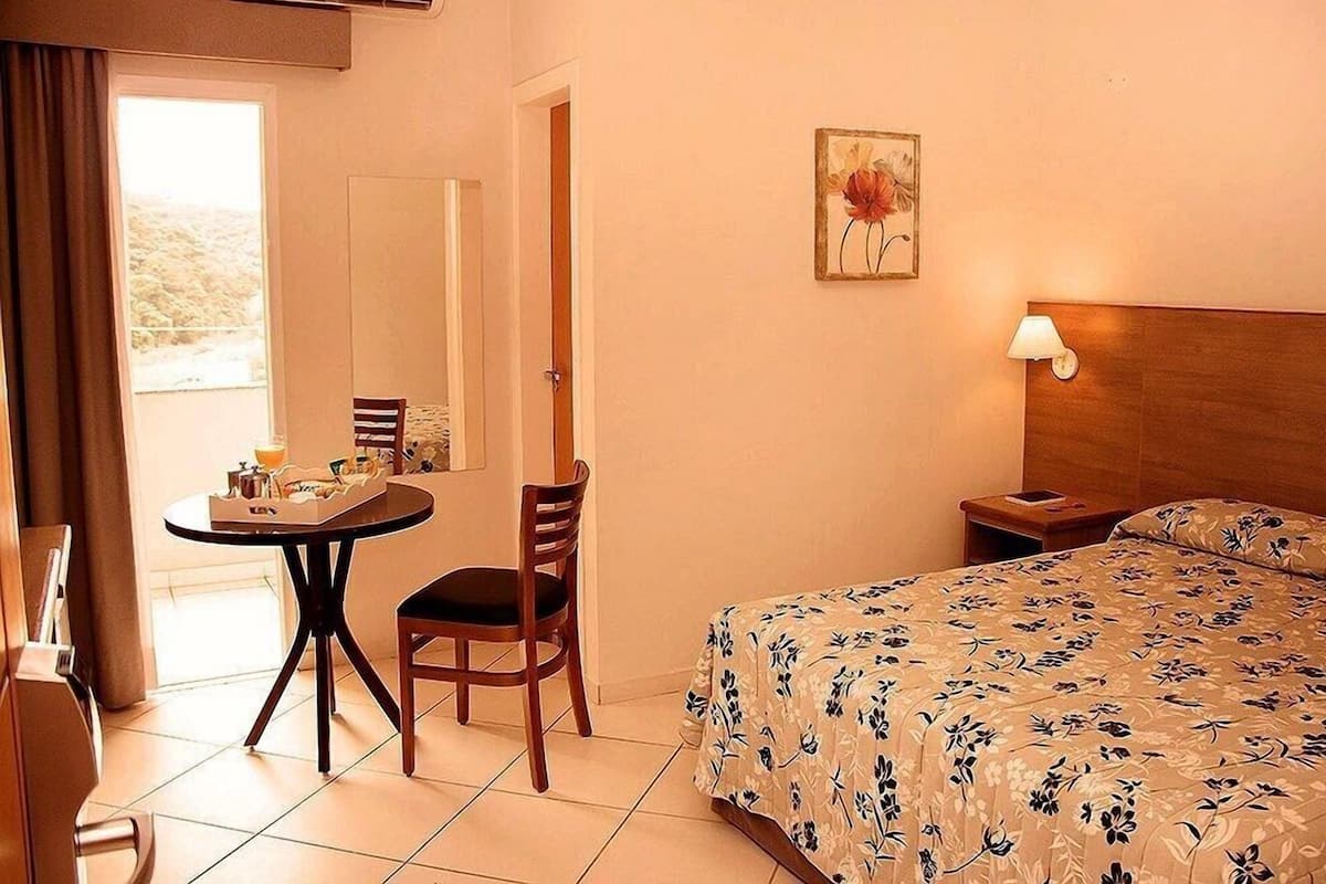 A hotel room with a bed, a table with chairs, a lamp, and a painting on the wall.