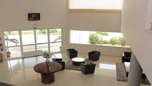 A lobby with a reception desk, seating area, and large windows offering views of the outdoors. - Lazuli Hotel (Itatiba)