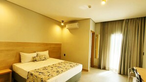 A hotel room with a large bed, a wooden headboard, a desk, and a window with curtains. - Lazuli Hotel (Itatiba)