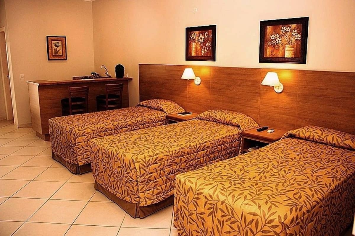 A hotel room with three single beds, a desk with two chairs, and two wall-mounted lamps.