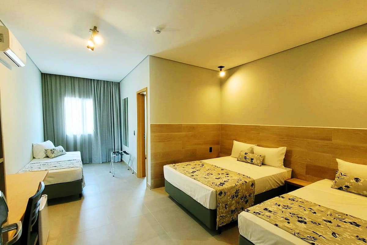 A hotel room with three beds, a desk, and a chair.