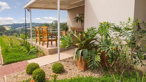 A covered outdoor seating area with chairs and a table, surrounded by potted plants and a view of the landscape. - Lazuli Hotel (Itatiba)