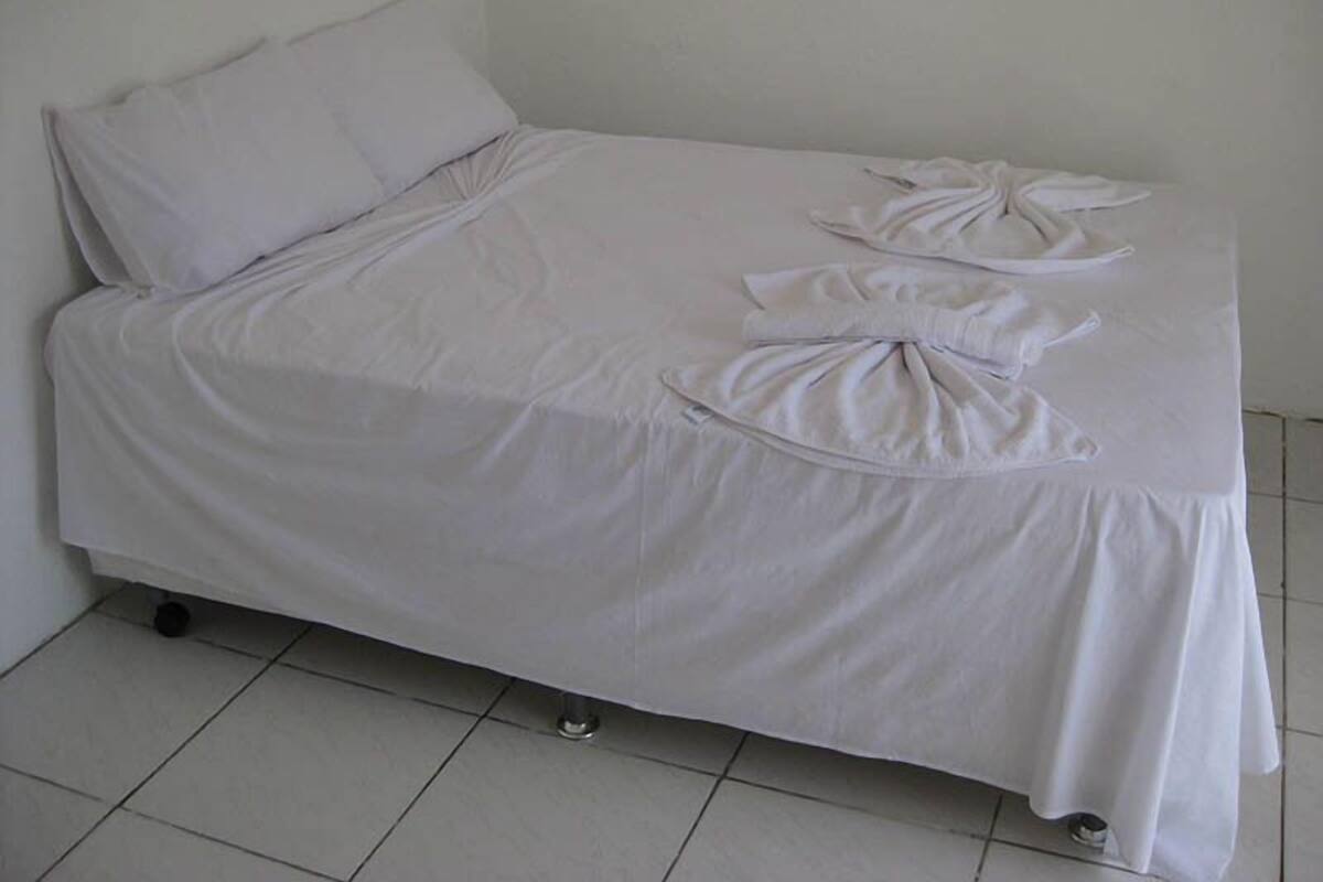 A single bed with a white bedspread and pillows, a pull-out drawer, and a small table with a white tablecloth.