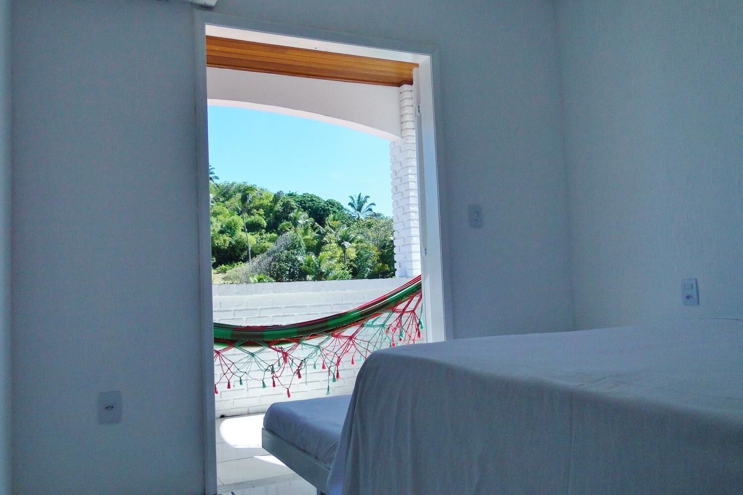 Un dormitorio con una cama, una hamaca y vistas al follaje exterior.