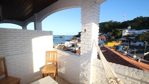 Un balcón con una silla y una mesa de madera, con vista a un pueblo costero con edificios y al mar.