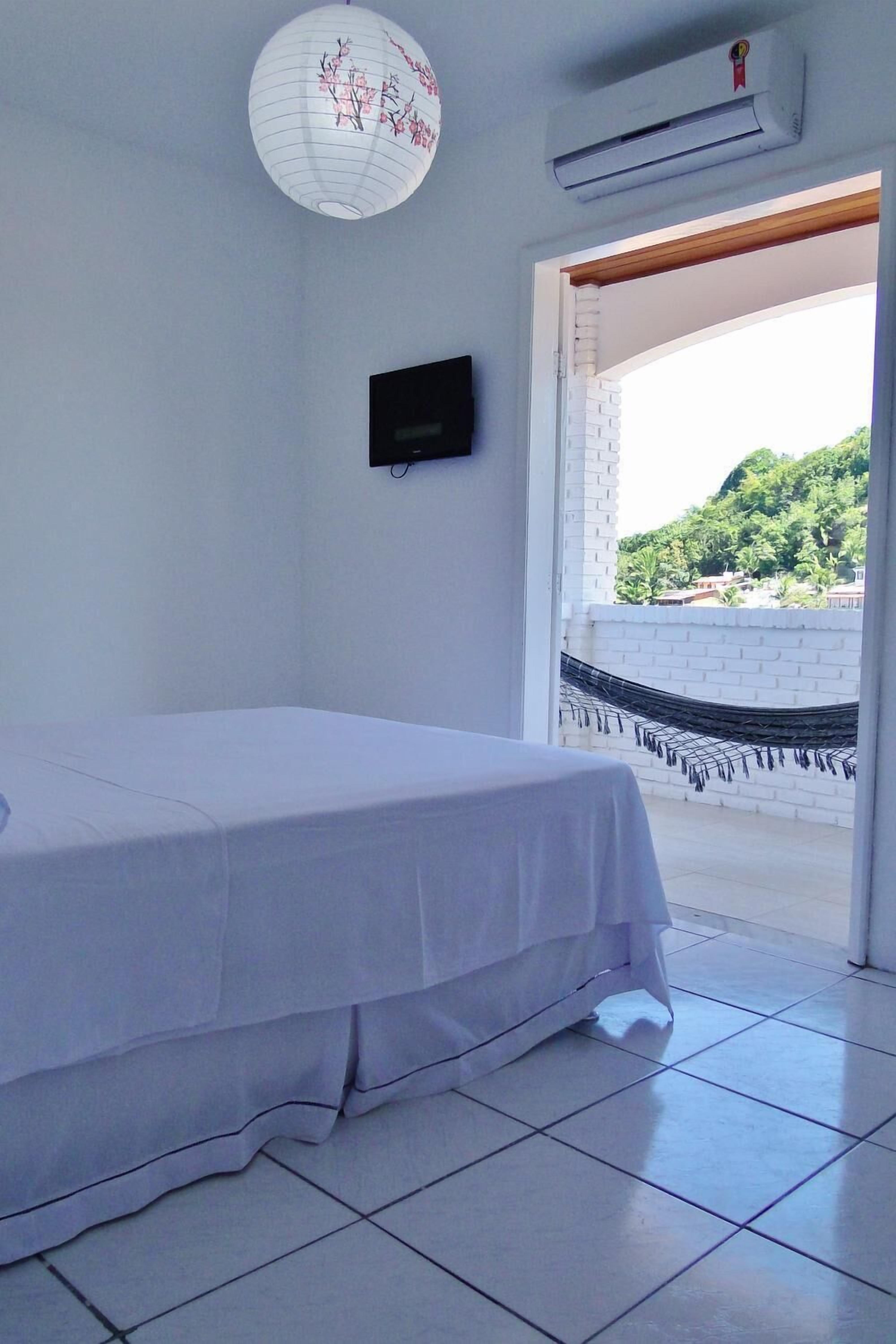 A bedroom with a bed, a TV, a hanging lantern, and a view of a hammock outside.