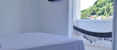 A bedroom with a bed, a TV, a hanging lantern, and a view of a hammock outside.