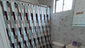 Une salle de bain avec un rideau de douche à motifs, des toilettes, un lavabo et une fenêtre.