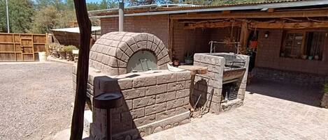 A stone oven with a chimney, a brick wall, and a wooden fence in a backyard.