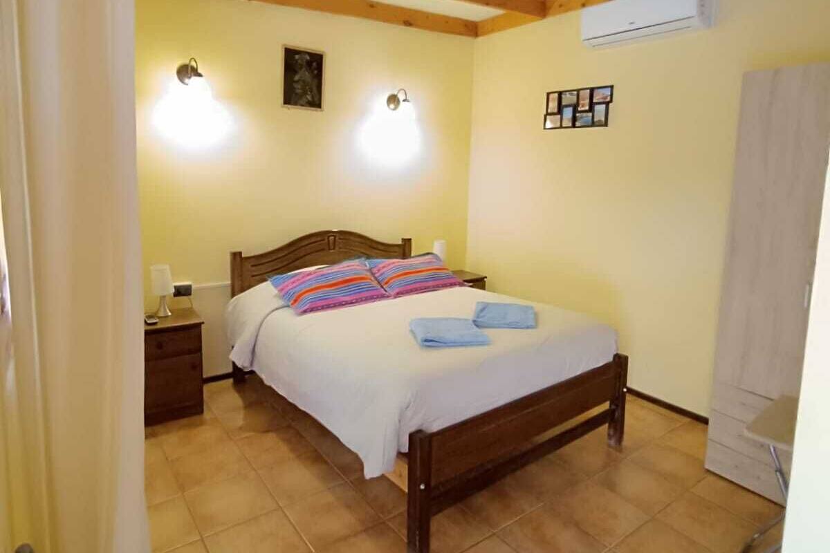 Une chambre à coucher avec un lit en bois, une table de chevet, un climatiseur fixé au mur et un sol carrelé.