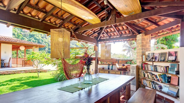A wooden bar area with a view of a lush garden and a bookshelf filled with books.