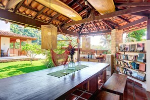 A wooden bar area with a view of a lush garden and a bookshelf filled with books. - Boutique Hotel Carpe Diem (Paraty)