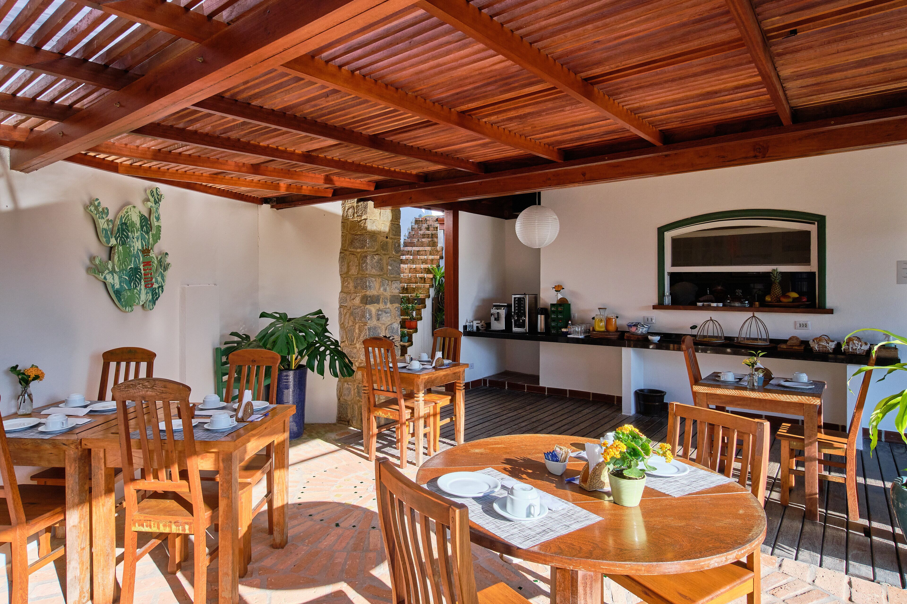 A wooden dining area with tables and chairs, a stone pillar, and a kitchen area with a window and counter.
