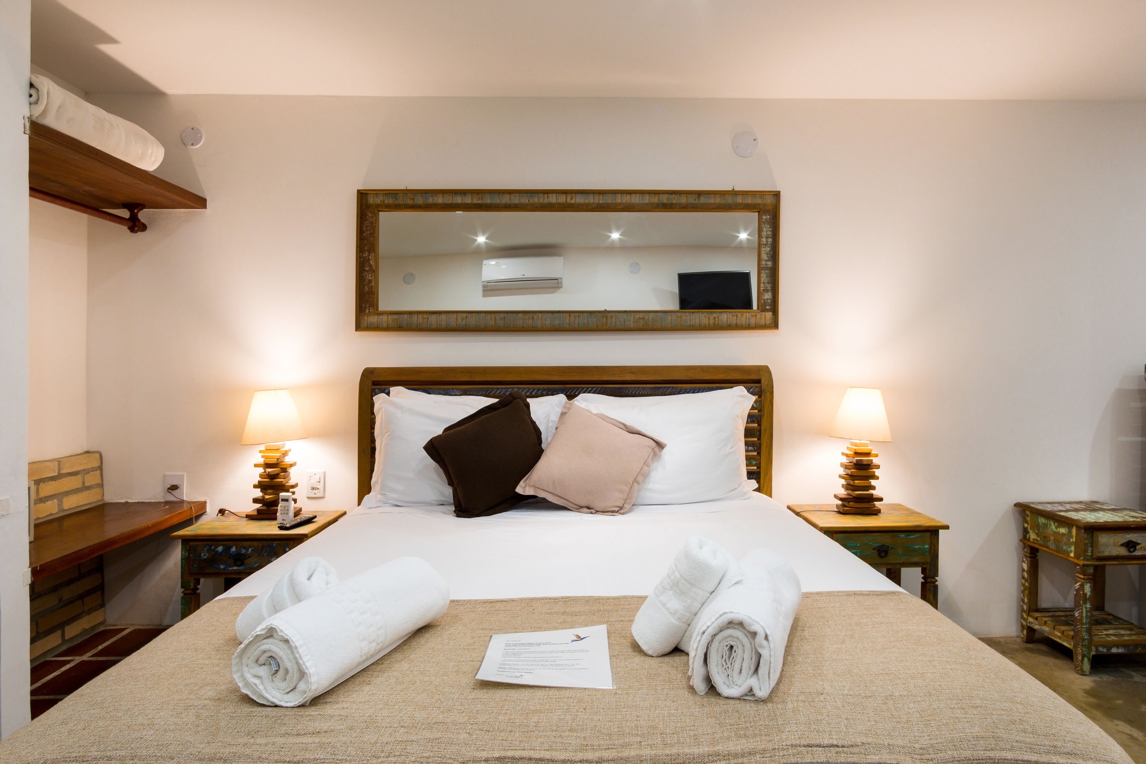 A neatly made bed with white linens, two bedside lamps, a wooden headboard, and a mirror above the bed.
