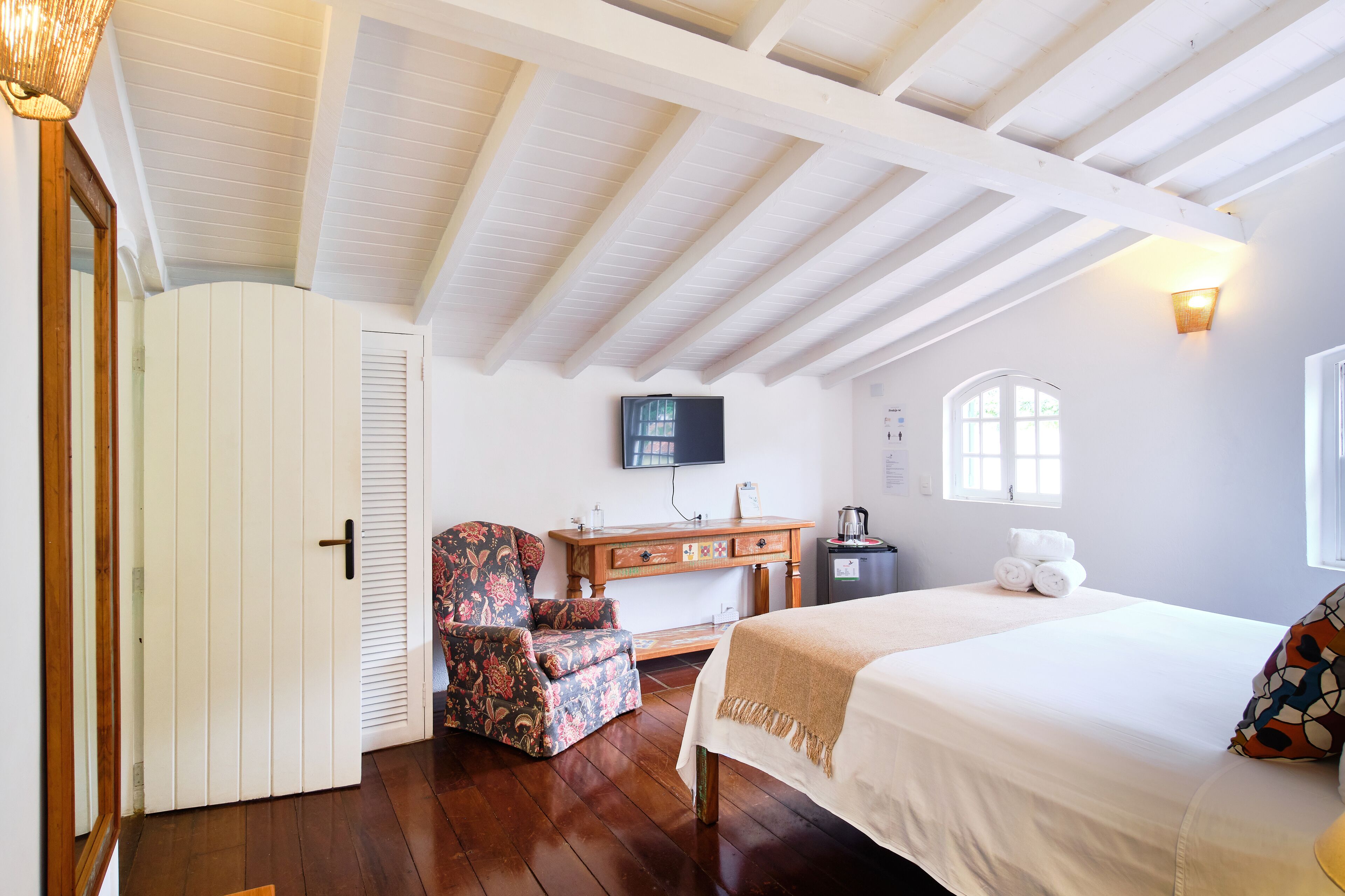 A bedroom with a wooden ceiling, a bed, a chair, a desk, a television, and a window.