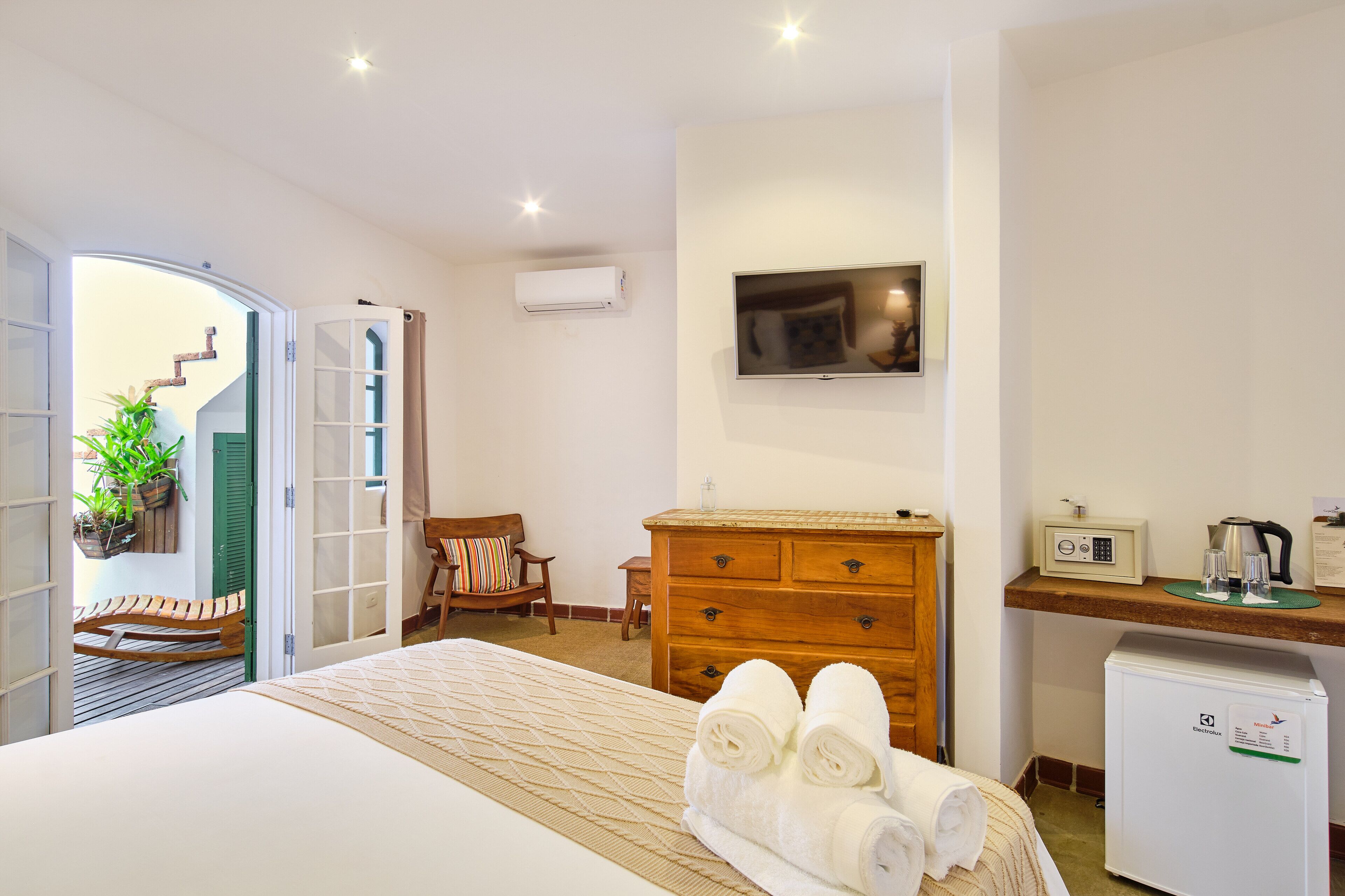 A hotel room with a bed, a wooden dresser, a TV, a desk with a coffee maker, and a refrigerator.
