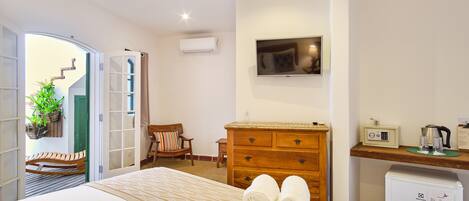 A hotel room with a bed, a wooden dresser, a TV, a desk with a coffee maker, and a refrigerator.