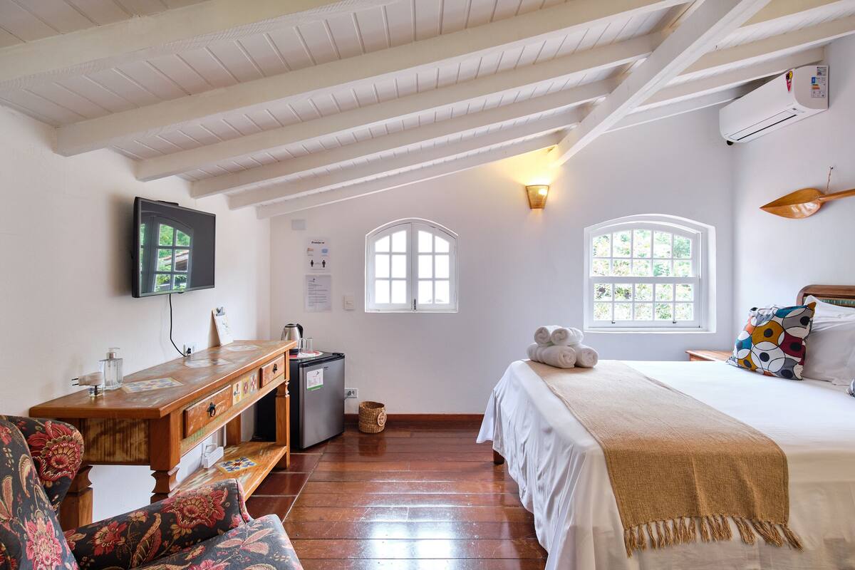 A bedroom with a bed, a wooden desk, a television, and two windows.