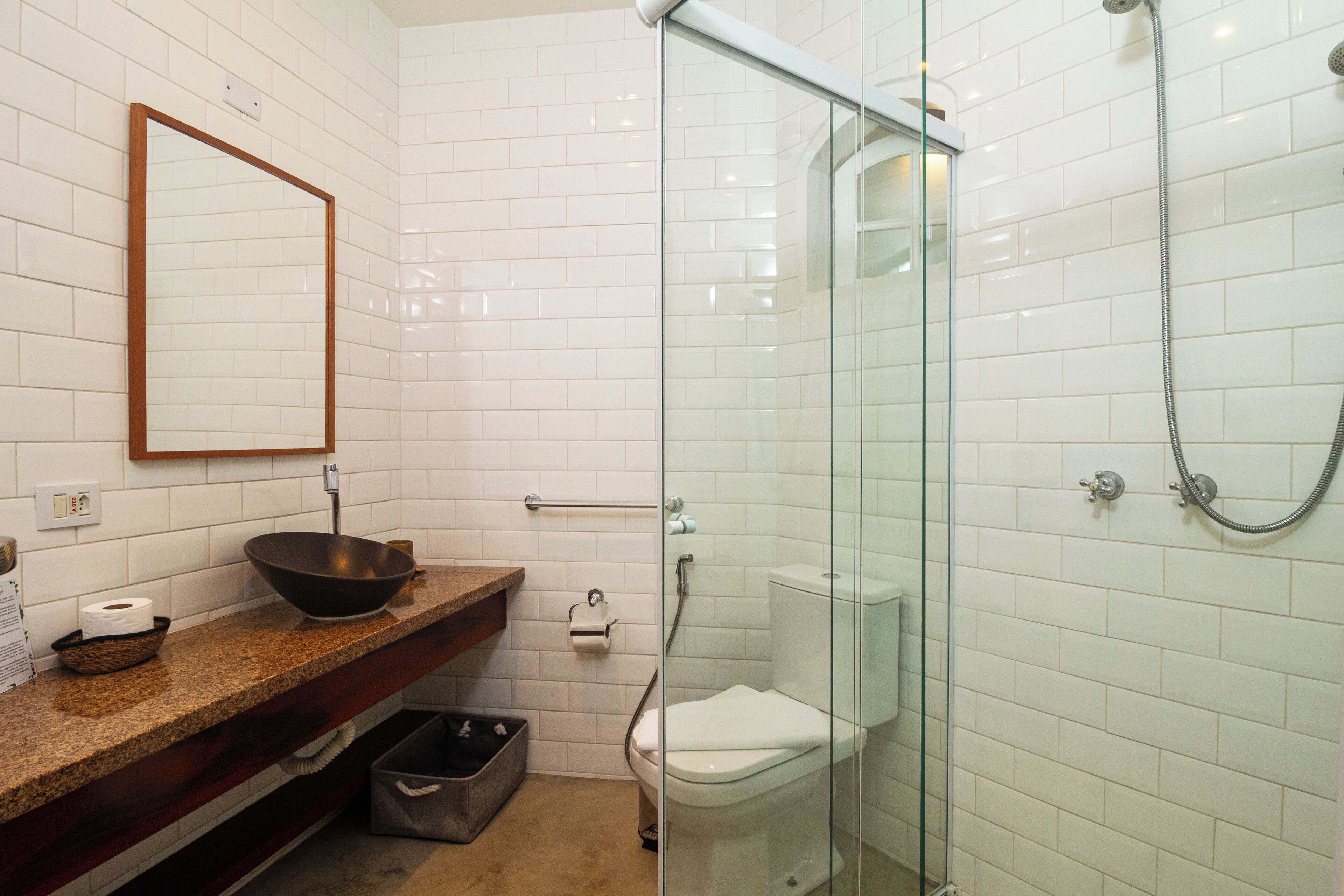 Un baño moderno con cabina de ducha de vidrio, tocador de madera y pared con azulejos blancos.