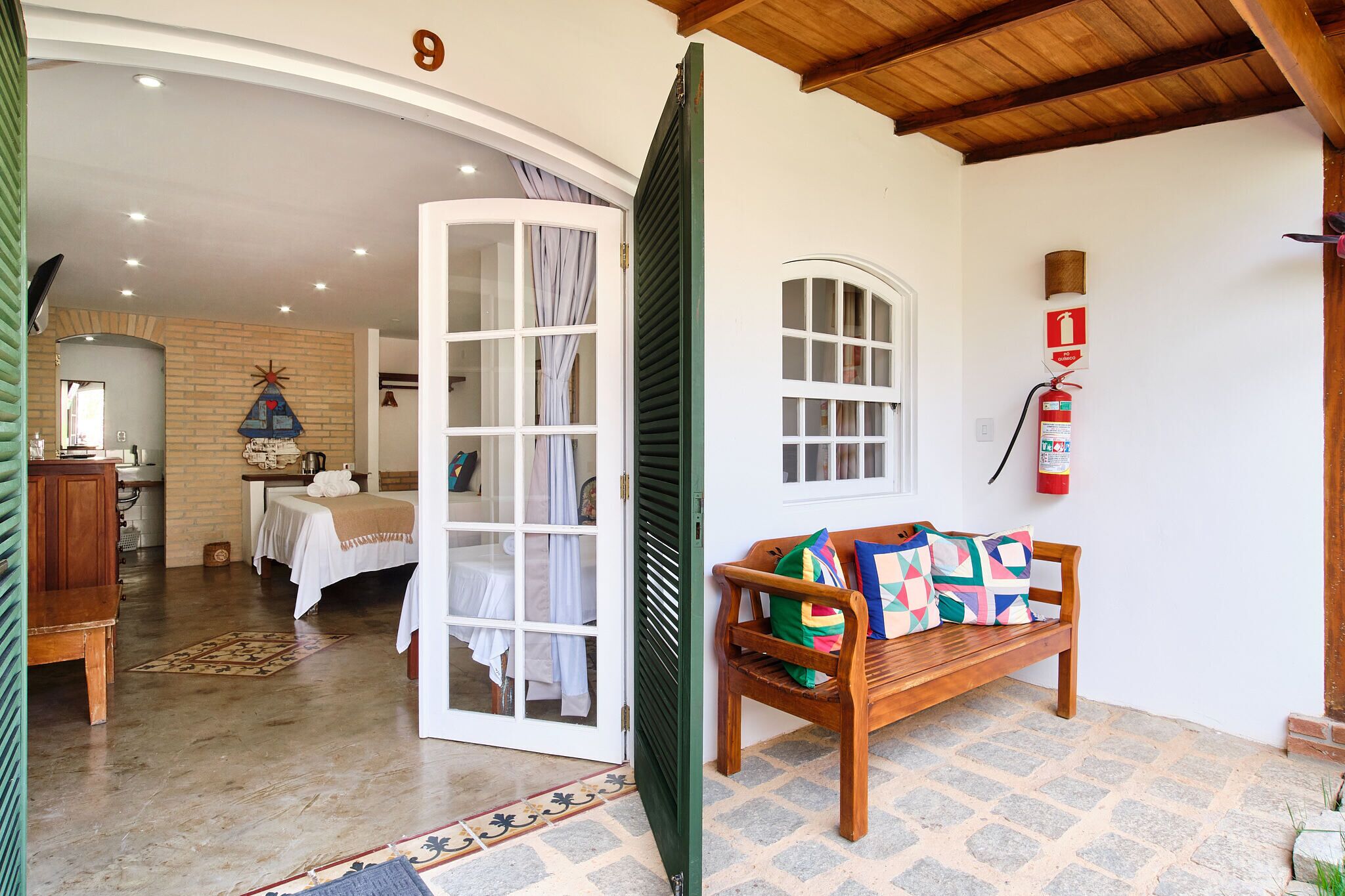 A cozy room with a wooden bench, a bed with white linens, a small table, and a door leading to another room.