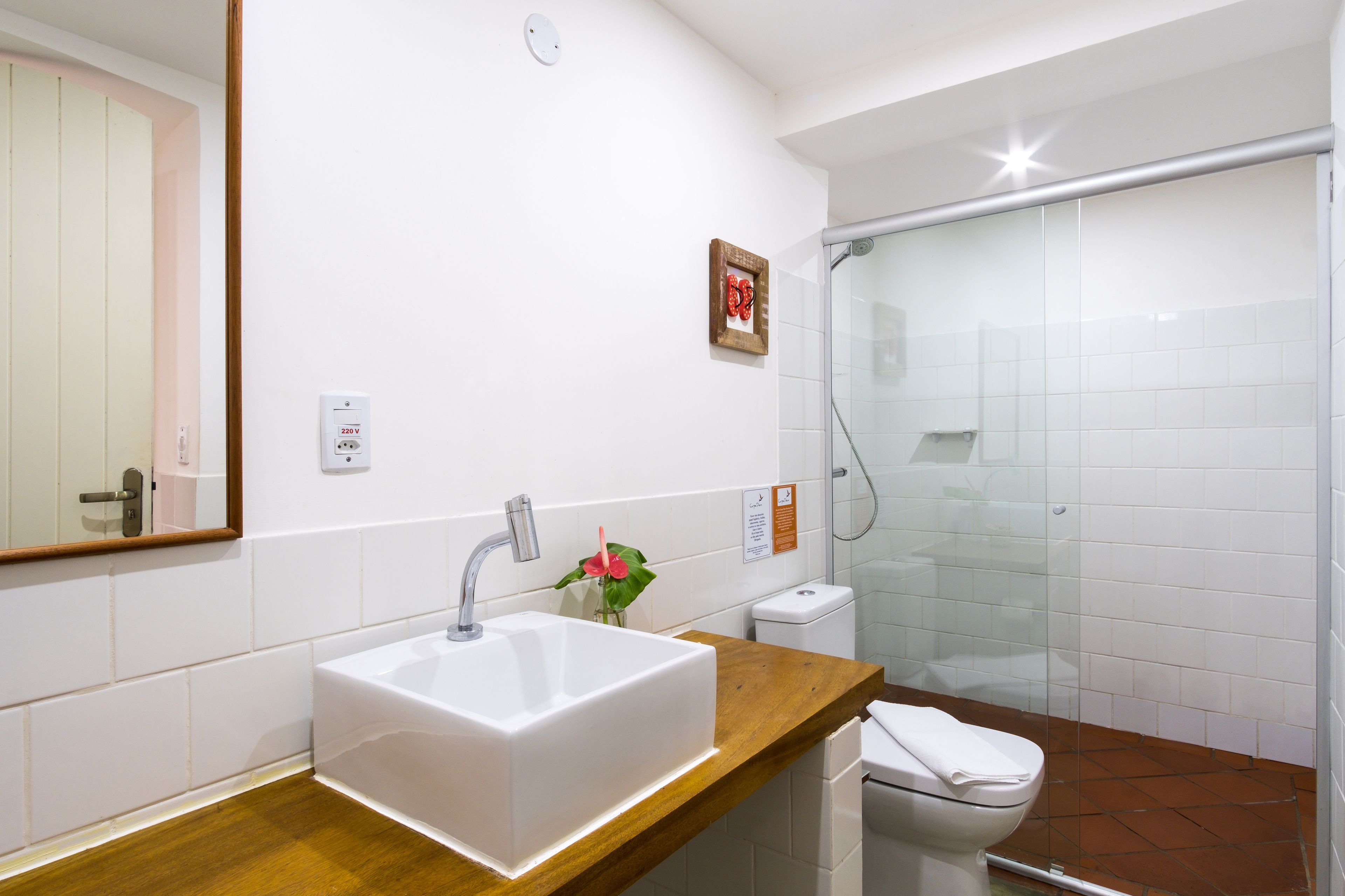 A bathroom with a white sink, a wooden countertop, a glass shower enclosure, and a white toilet.
