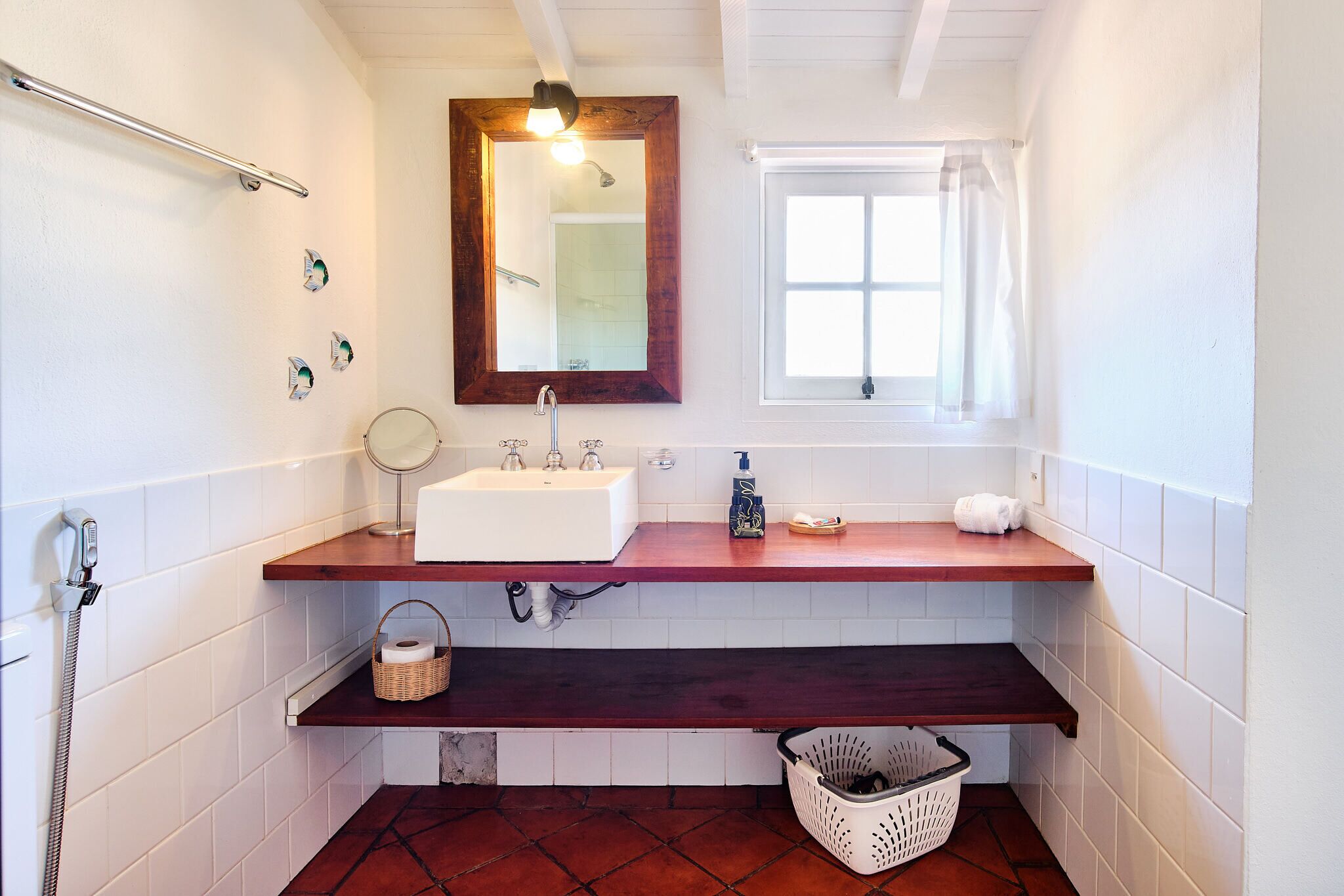 A bathroom with a white sink, wooden countertop, mirror, towel rack, window, and a shower area.