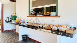 A breakfast bar with various food items and beverages, a window with a view, and a wooden floor. - Boutique Hotel Carpe Diem (Paraty)