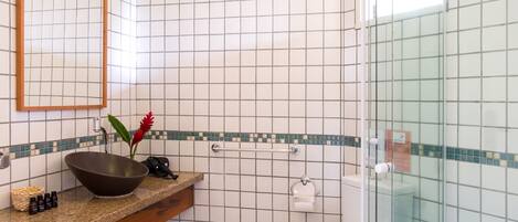 A bathroom with a glass shower enclosure, a white toilet, a wooden vanity with a large sink, and a mirror.