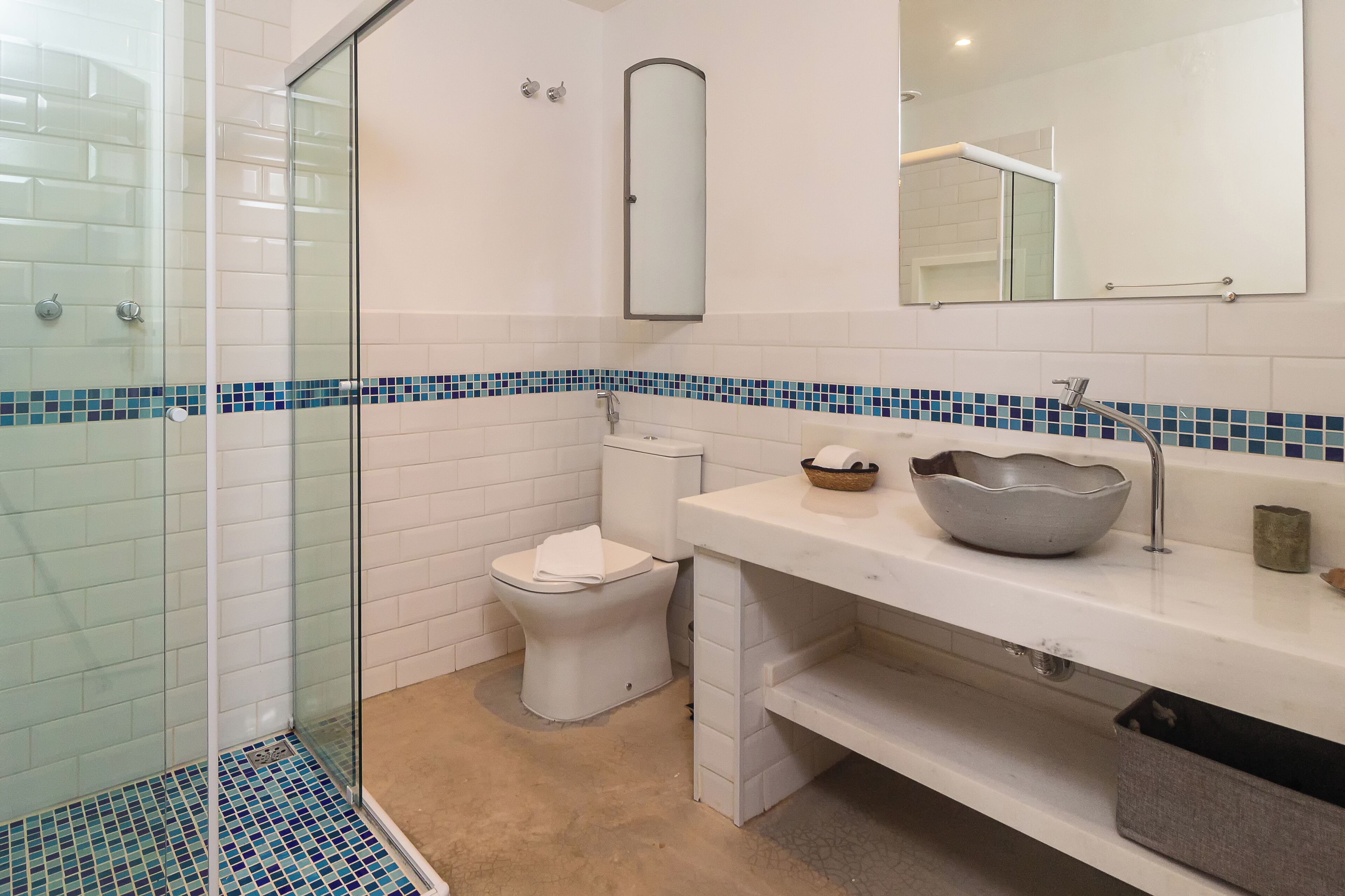 A bathroom with a glass shower enclosure, a toilet, a sink with a bowl, and a mirror.
