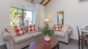 A living room with a beige sofa set, a wooden coffee table, and a dining area with a table and chairs. - Anzac Court Motel (Auckland)