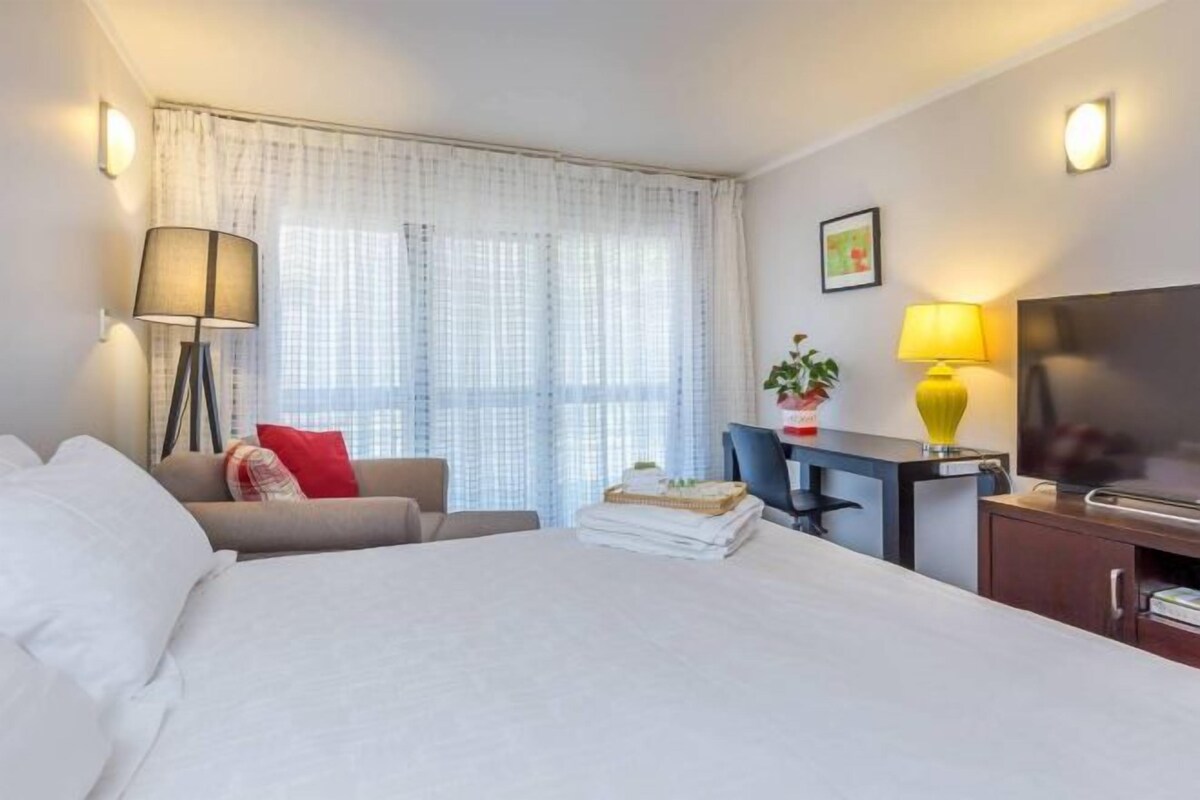 A hotel room with a bed, a desk, a chair, a TV, and a window with curtains.