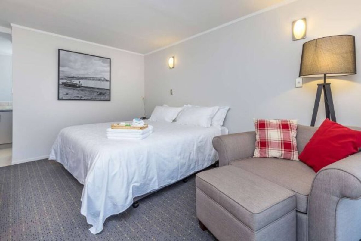 A bedroom with a bed, a bedside table, a lamp, a couch, and a wall-mounted picture.