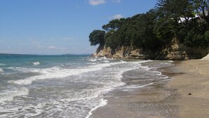 A beach with waves, a sandy shore, and a cliff with trees. - Anzac Court Motel (Auckland)