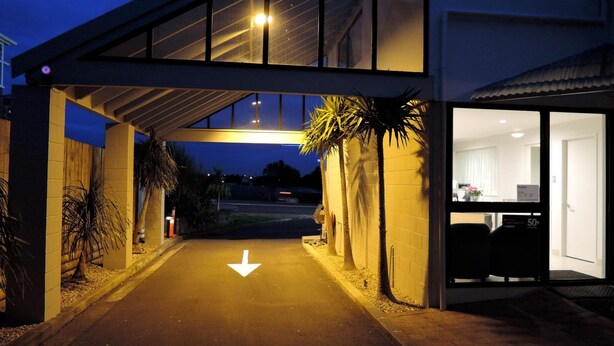 A modern building entrance with a clear pathway marked by a downward arrow, a covered walkway, and a visible office area with a computer monitor. - Anzac Court Motel (Auckland)